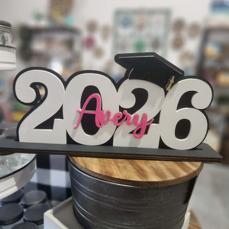 Graduation-themed decorative item with '2026' and 'Avery' on a blurred background