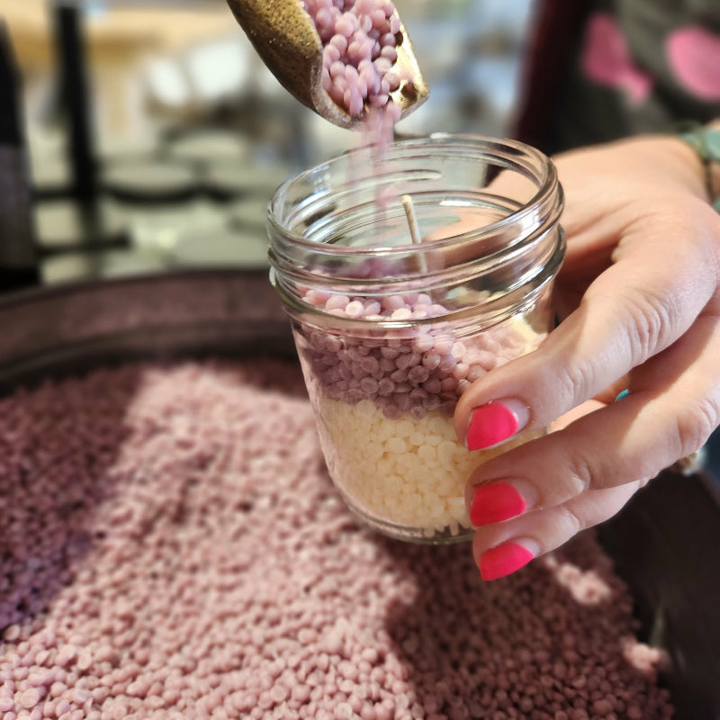 Hand pouring pink and white wax beads into a glass jar.