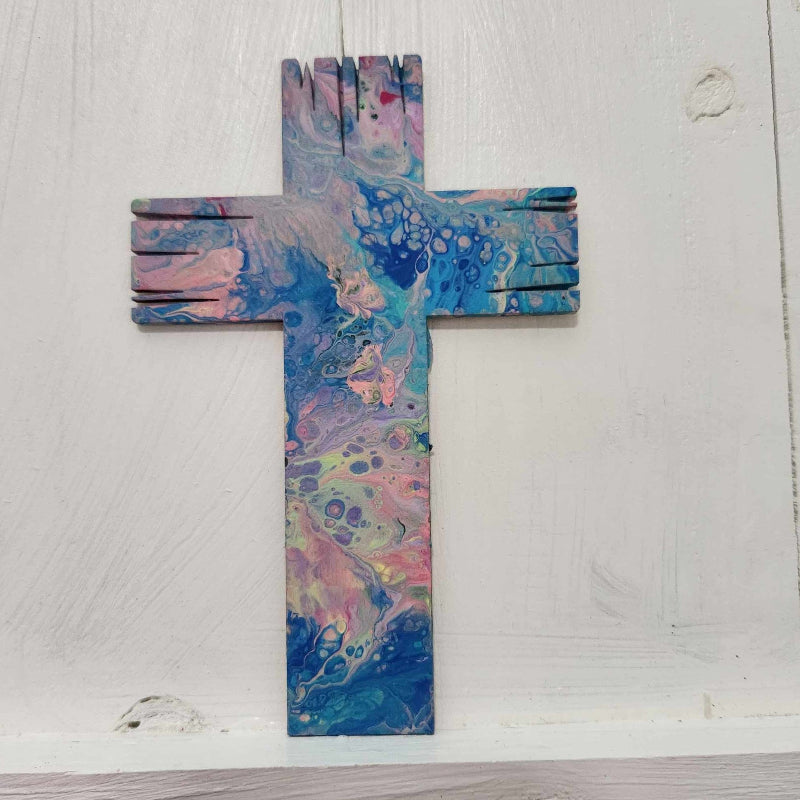 A wooden cross with a paint pour design in blue and pink hues, displayed against a white background.