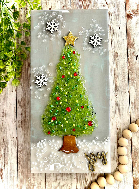 Decorative Christmas canvas with a tree, star, and 'Joy' text on a wooden surface with crushed glass.