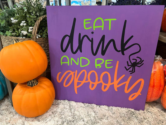 Purple sign with Halloween text 'Eat drink and be spooky' surrounded by pumpkins.