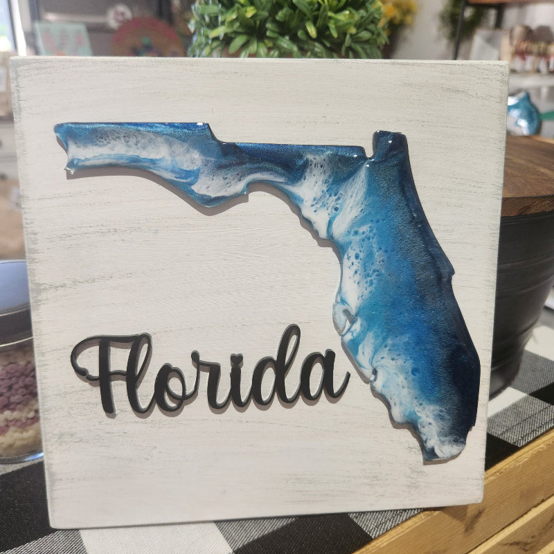 Decorative sign with a blue outline of Florida and 'Florida' text on a white background.