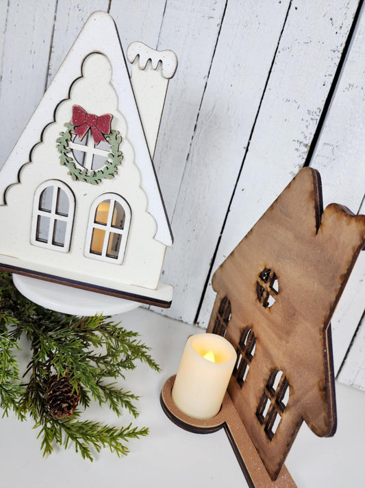 Decorative house-shaped candle holder with a candle on a wooden surface.