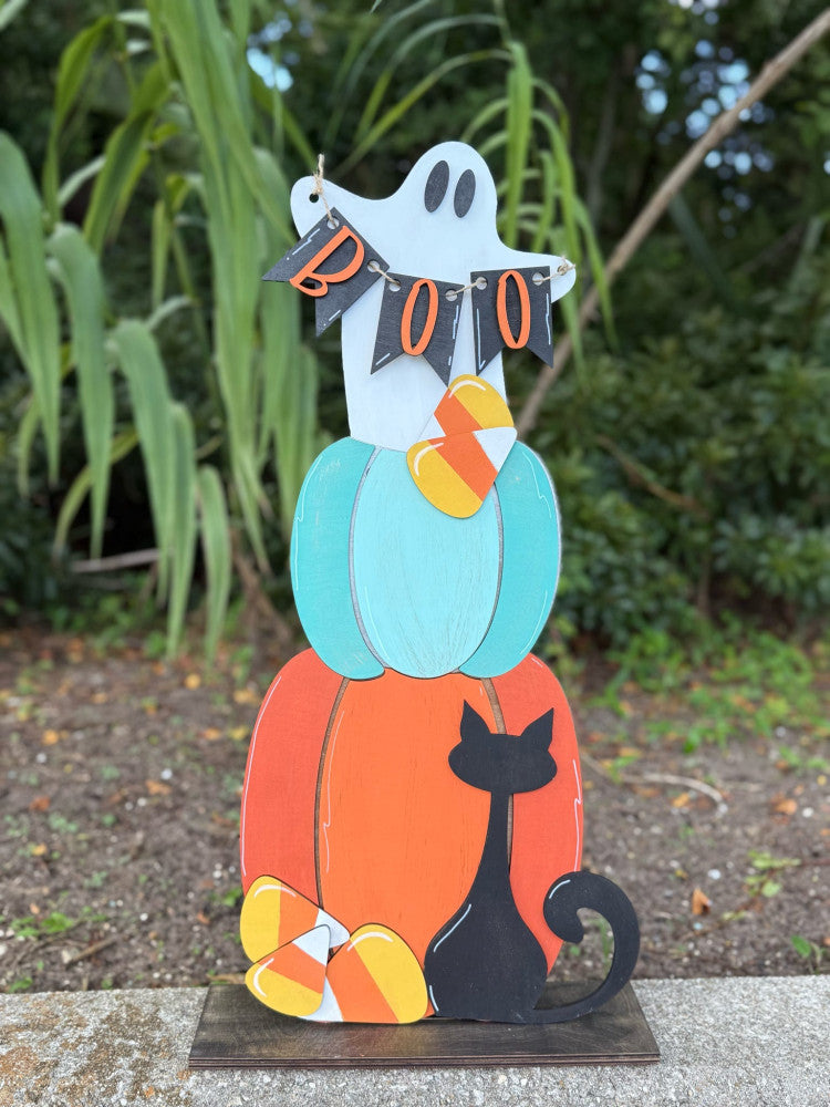 Halloween-themed decorative stand with a ghost, pumpkin, and black cat on a concrete surface.