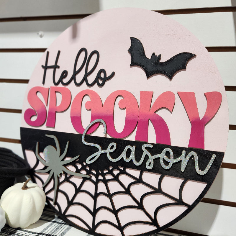 Decorative sign with 'Hello Spooky Season' text and Halloween elements on a wooden background.