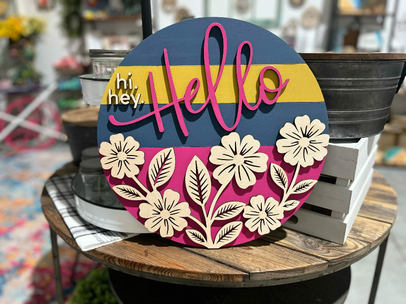 Decorative sign with floral designs and 'hello' text on a wooden surface.