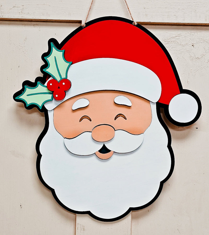 Decorative cutout of Santa Claus face with a red hat and holly leaf on a wooden background