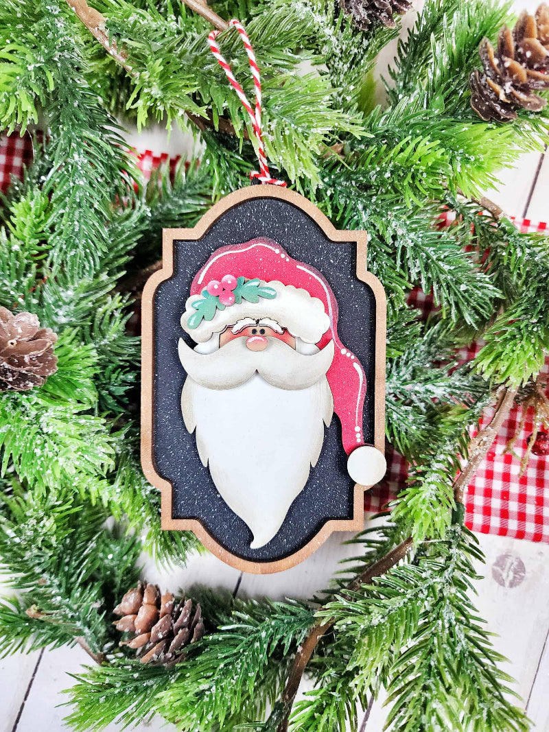 Decorative Christmas ornament of a Santa Claus face on a tree with pine cones and red checkered fabric.