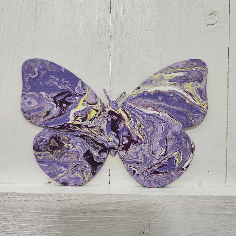 A wooden cutout in the shape of a butterfly with a paint pour design in purple and yellow hues.