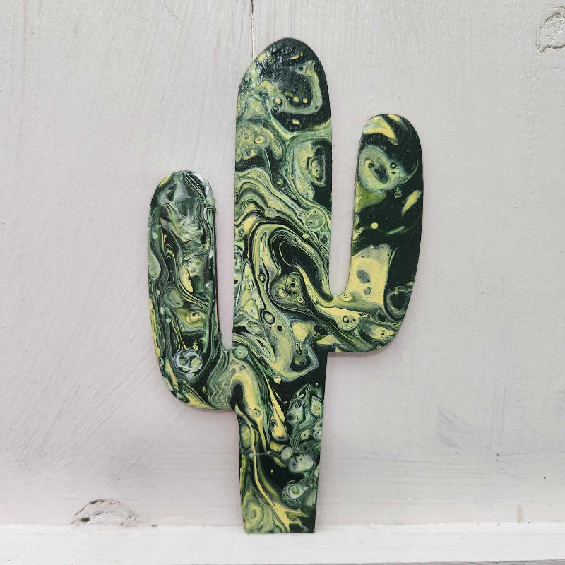 A wooden cutout in the shape of a cactus with a paint pour design in green and black hues, resembling a desert-inspired pattern.