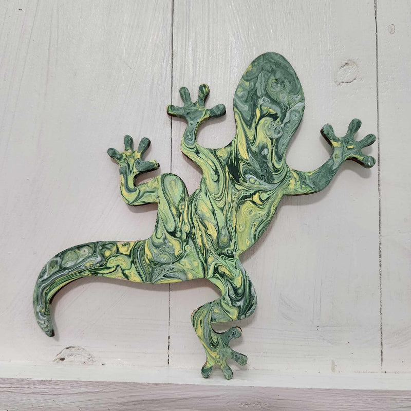 A wooden cutout in the shape of a gecko with a vibrant green and yellow paint pour design.