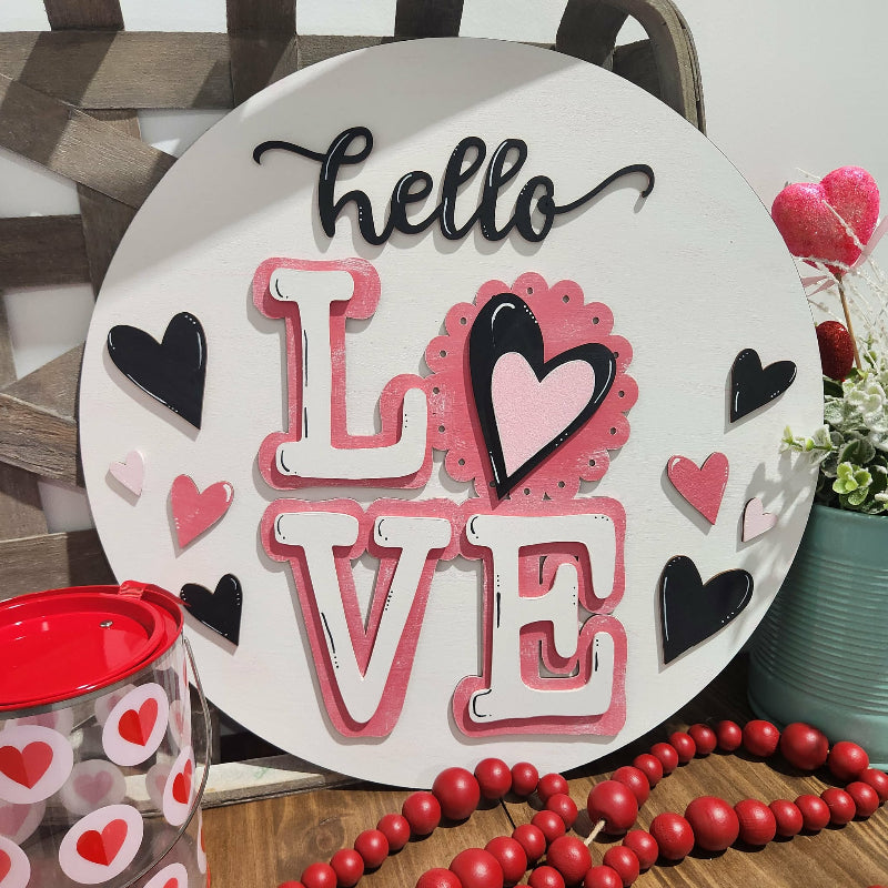 Decorative sign with 'hello LOVE' text and heart designs on a wooden surface.