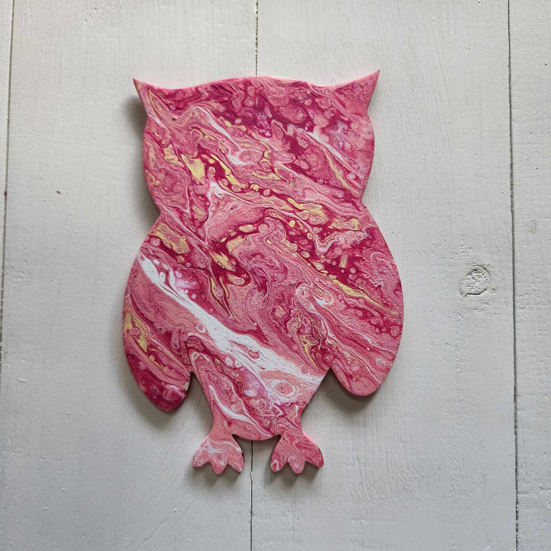 A wooden cutout in the shape of an owl with a pink marbled paint pour design.