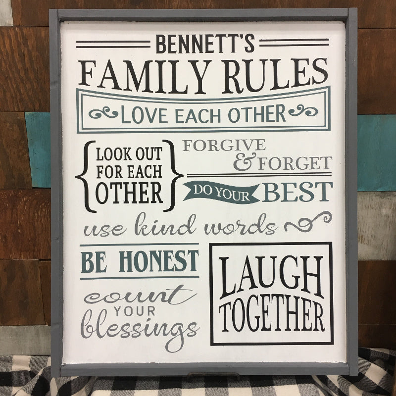 A decorative plaque with a black and white text that reads 'BENNETT'S FAMILY RULES' and various phrases such as 'LOVE EACH OTHER', 'FORGIVE & FORGET', 'DO YOUR BEST', 'USE KIND WORDS', 'LAUGH & SING'.