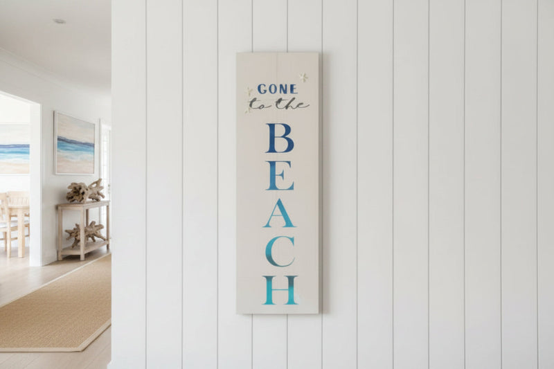 A vertical wooden plank with the text 'GONE to the BEACH' written in a blue font, against a white background, meant as a decorative piece for a gallery or home setting.