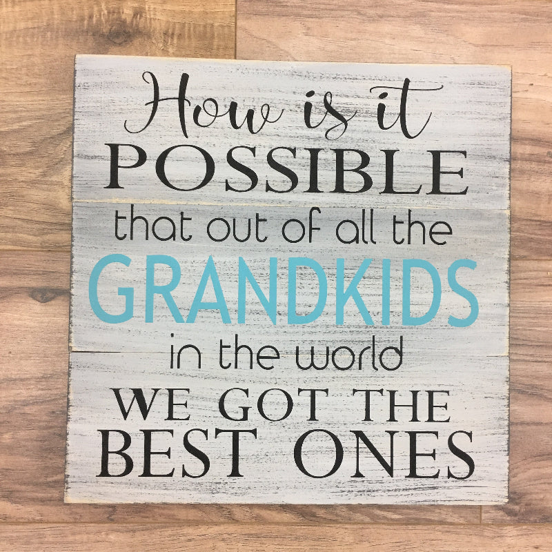 A square-shaped wall art with a wooden background and black text that reads 'HOW IS IT POSSIBLE THAT OUT OF ALL THE GRANDKIDS WE GOT THE BEST ONES?' with a blue accent on the text.
