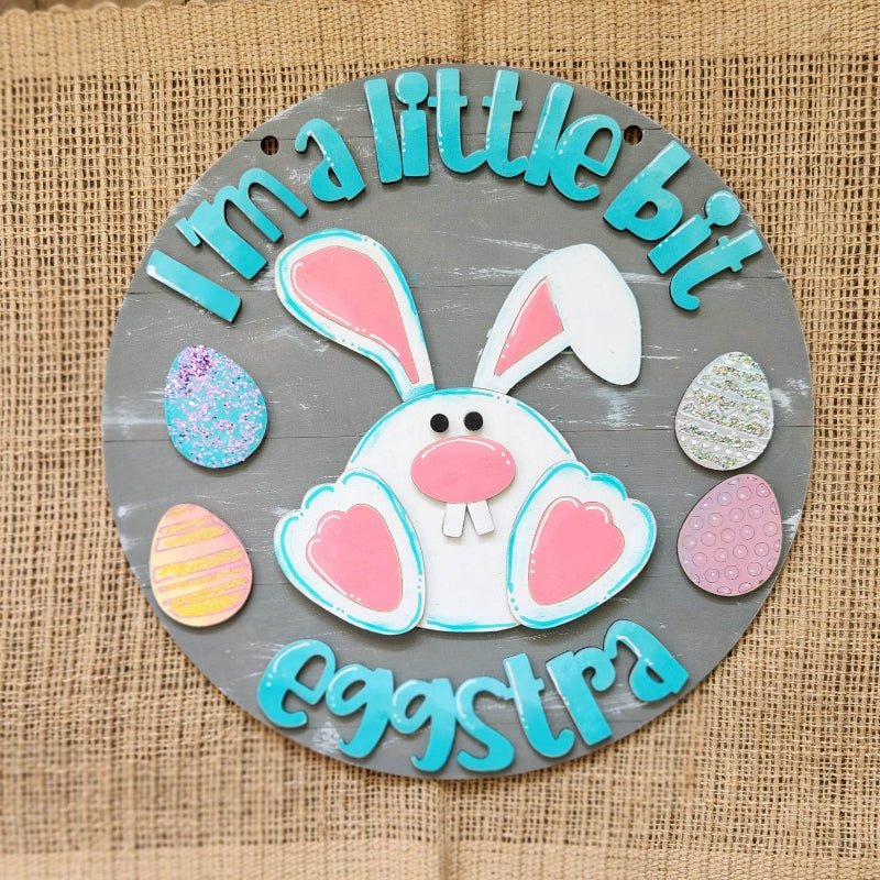 white bunny on a gray background with colorful eggs around the desgin that says I'm a little bit eggstra