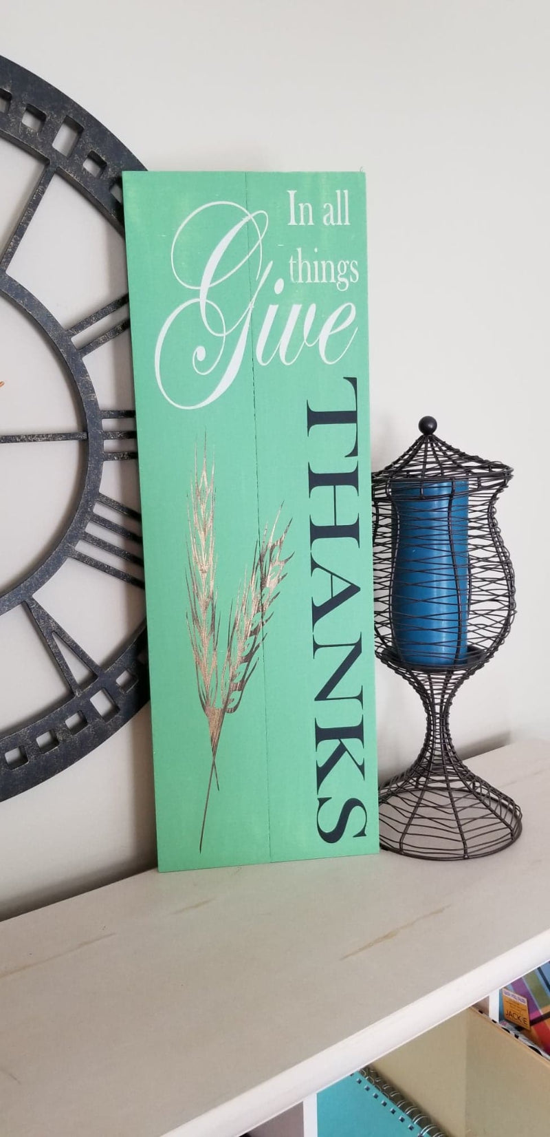 A green plank design with the text 'GIVE THANKS' and a wheat illustration, typically used as seasonal decoration for Thanksgiving.