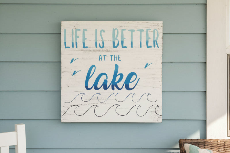 Life is better at the lake written in blue with waves at the bottom on a white wooden square