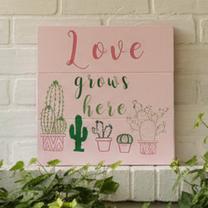 A square-shaped pink artwork with the text 'LOVE GROWS HERE' surrounded by cacti illustrations.
