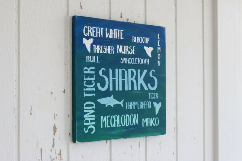 A square-shaped decorative plaque with a blue background featuring text and illustrations related to various shark species, such as 'Great White', 'Blacktip', 'Thresher Nurse', 'Snaggletooth', 'Hammerhead', and 'Mako'.