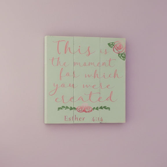 A square-shaped wall art with a green background, featuring the text 'This is the moment for which you were created' in pink and green, with additional decorative elements.