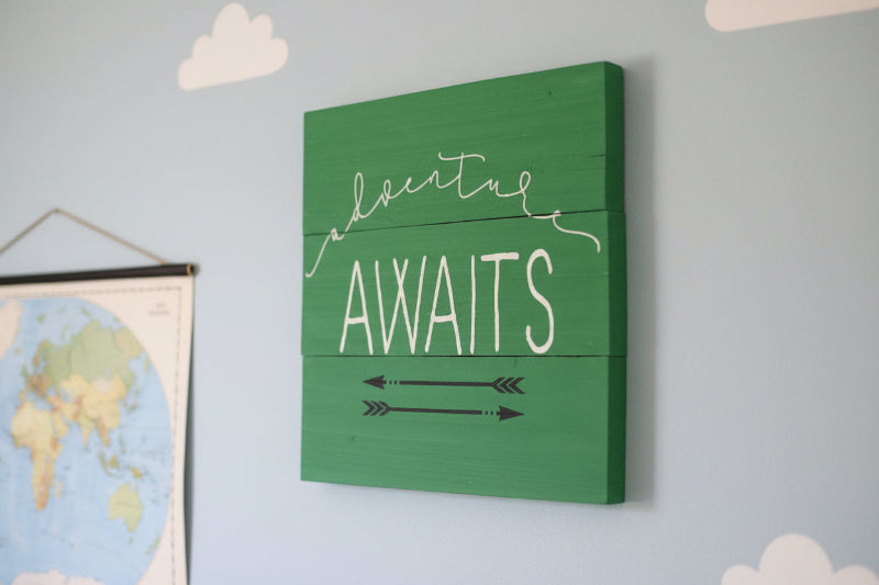Adventure Awaits written on a green background with 2 arrows underneath painted on in black