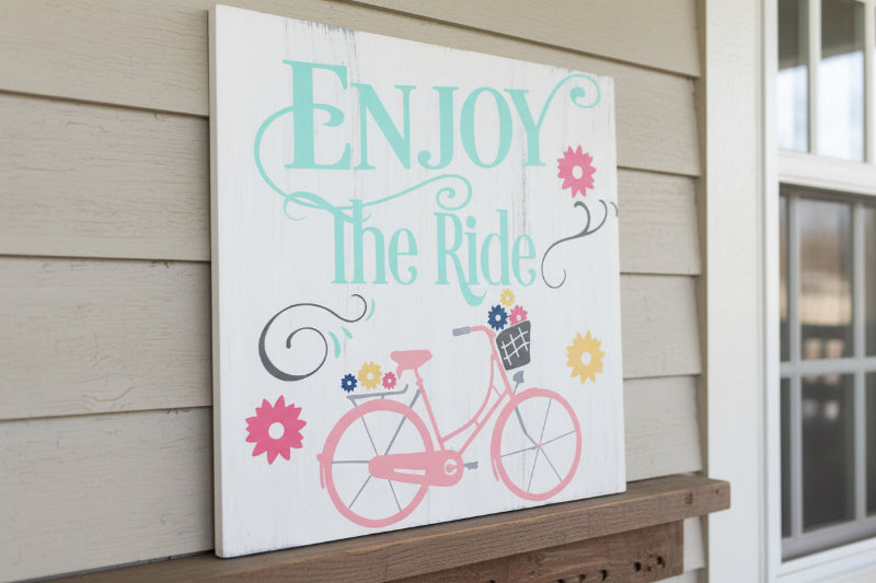 Bicycle with a basket of flowers set on a white wooden square and Enjoy the Ride written onthe top