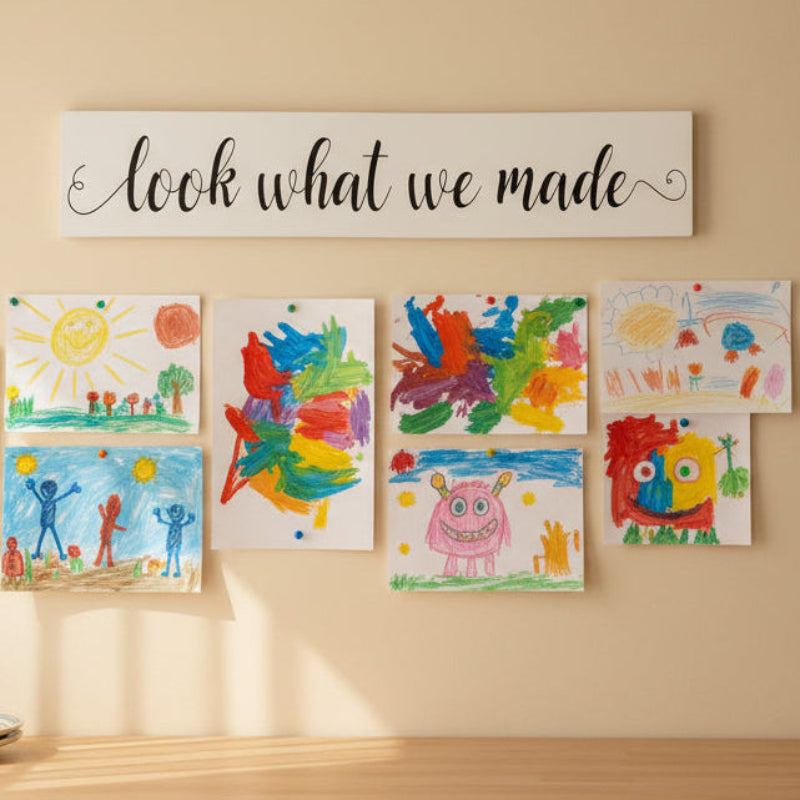 A white plank design with the text 'LOOK WHAT WE MADE' in black, hanging on a tile wall.