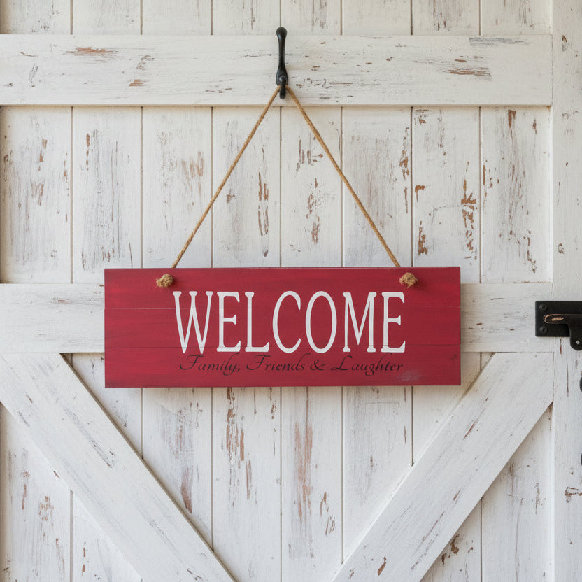 A red wooden plank-style sign with the text 'Welcome' and 'Friends, family, and laughter' in a white distressed font.
