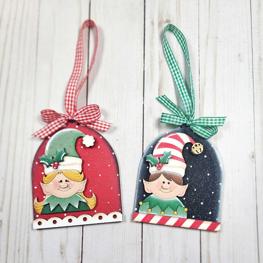 Two Christmas-themed elf ornaments with ribbons on a wooden surface