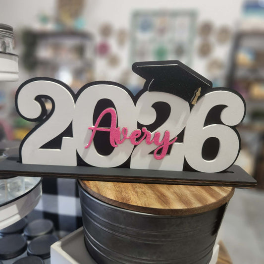 Graduation-themed decorative item with '2026' and 'Avery' on a blurred background