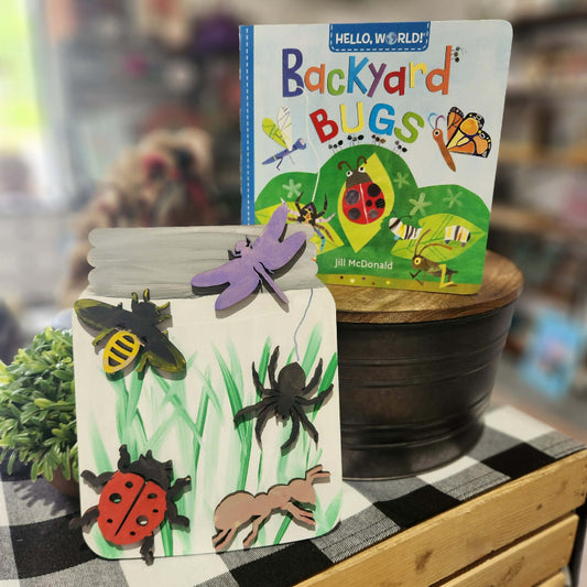 Children's book titled 'Backyard Bugs' by Jill McDonald on a checkered tablecloth with a jar of ladybugs.