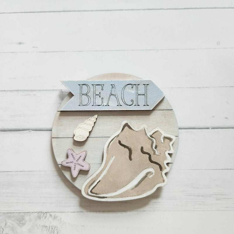 Decorative wall art with a shell, starfish, and 'Beach' sign on a wooden background