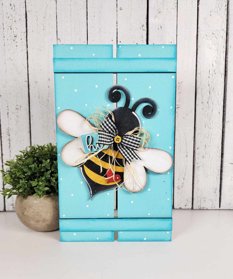 A decorative wooden pallet sign with a colorful bee design, mounted on a blue background with white dots.