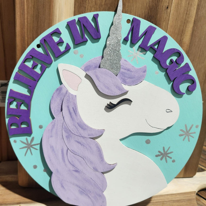Decorative sign with a unicorn and 'Believe in Magic' text on a wooden background