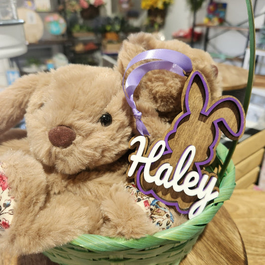 Easter Bunny in a basket with a decorative Easter basket tag labeled 'Haley' in a store setting.