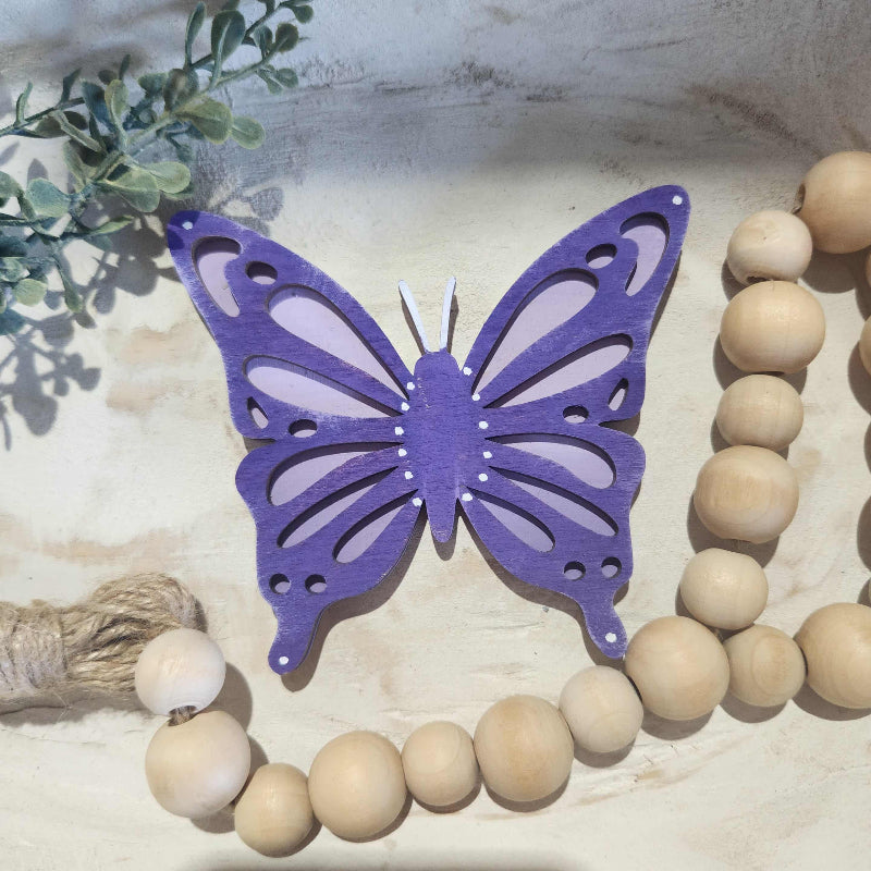 Purple butterfly ornament on a wooden bead and leaf background