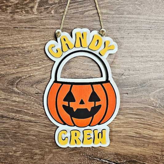 Halloween-themed decorative sign with a pumpkin and 'Candy Crew' text on a wooden background