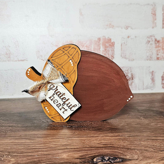 Wooden acorn with a decorative bow and tag on a wooden surface.
