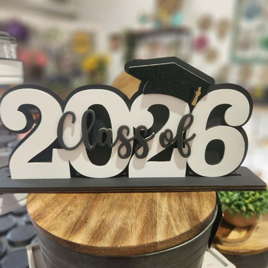 Decorative sign with '2026 Class of' and a graduation cap on a wooden surface.