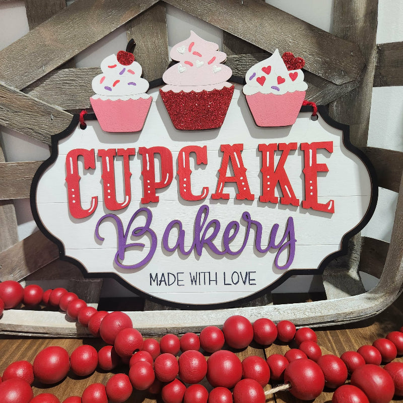 Decorative sign with 'Cupcake Bakery' text and cupcake illustrations on a wooden background.