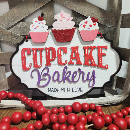 Decorative sign with 'Cupcake Bakery' text and cupcake illustrations on a wooden background.