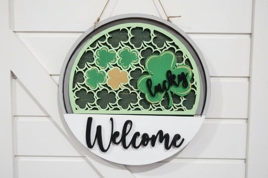 Decorative sign with shamrock designs and the word 'Welcome' on a wooden background.