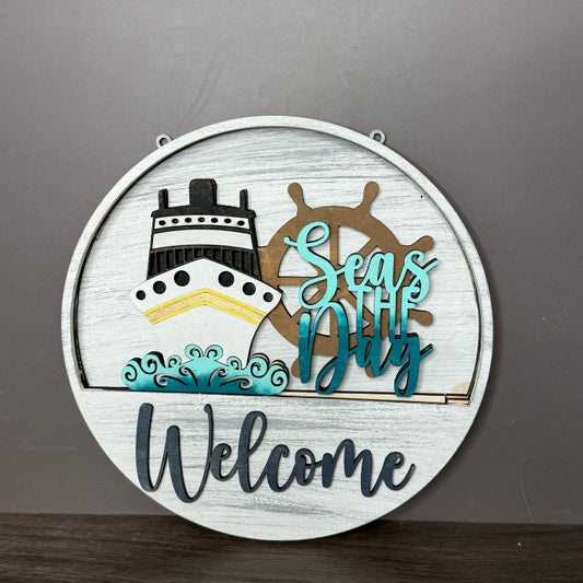 Decorative sign with a ship, steering wheel, and 'Seas the Day Welcome' text on a gray background.