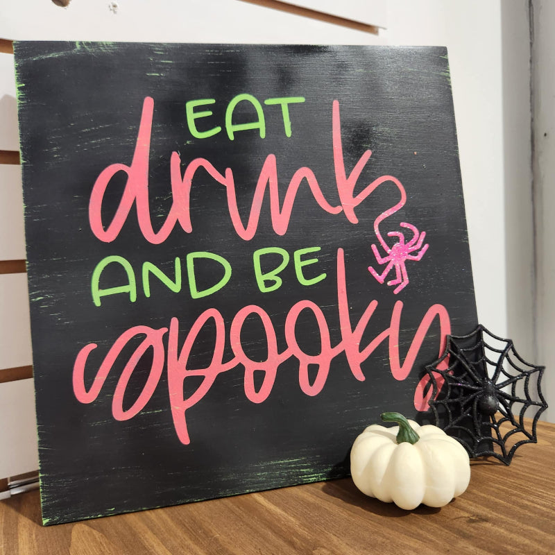 Halloween-themed sign with 'Eat, drink, and be spookin'' text on a black background.