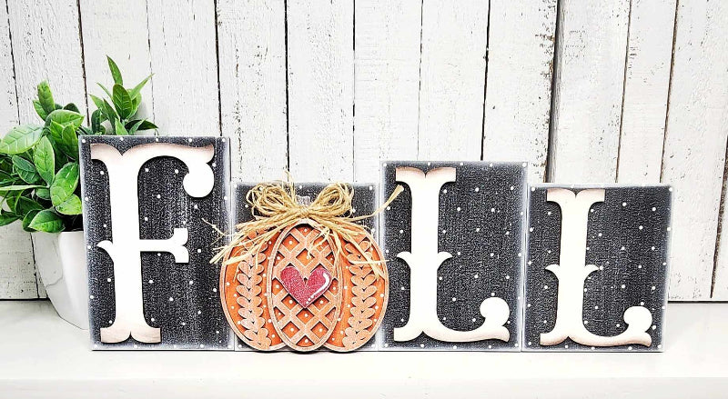 Decorative sign with 'FALL' letters and a pumpkin on a wooden background