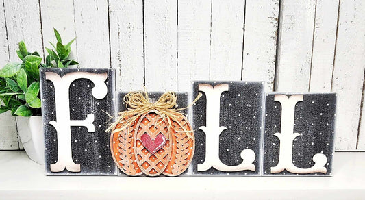 Decorative sign with 'FALL' letters and a pumpkin on a wooden background