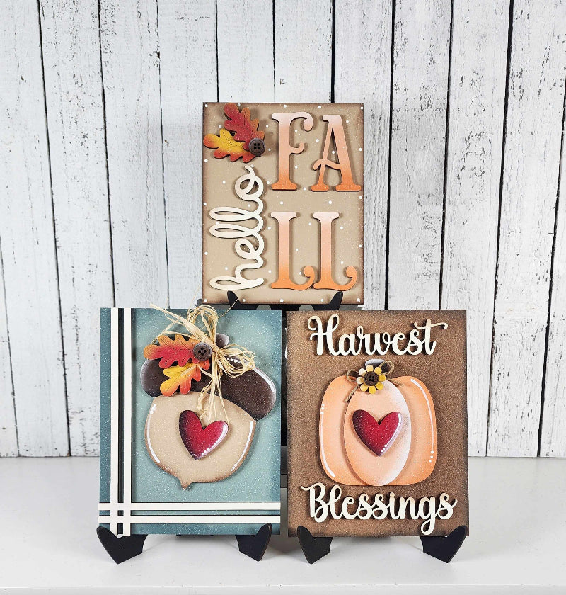 Three wooden signs with autumn-themed designs on a white background
