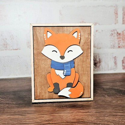 Wooden framed picture of a fox with a blue scarf on a wooden surface.